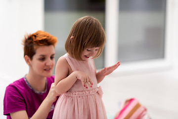 Image showing young mother helping daughter while putting on a dress