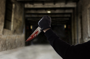 Image showing hand in glove with bloody knife over dark gateway