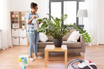 Image showing happy african woman spraying houseplants at home