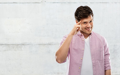 Image showing smiling young man pointing finger to his head