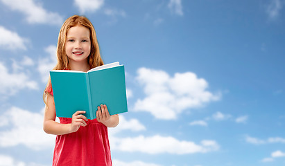 Image showing smiling red haired girl reading book over sky