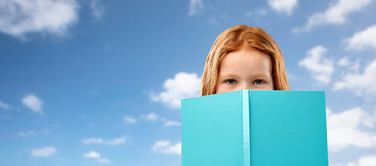 Image showing red haired girl hiding behind book over sky