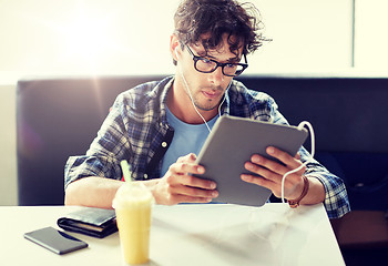 Image showing man with tablet pc and earphones sitting at cafe