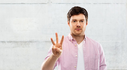 Image showing young man showing three fingers over grey