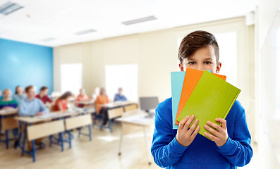 Image showing shy student boy hiding behind books at school
