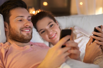 Image showing happy couple using smartphones in bed at night