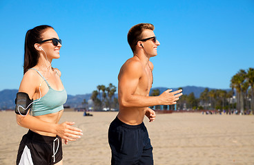 Image showing couple with phones and arm bands running on beach