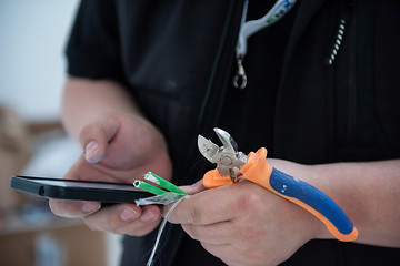 Image showing electrical engineer with wire and pliers in his hand using mobil