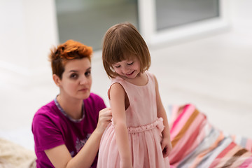 Image showing young mother helping daughter while putting on a dress