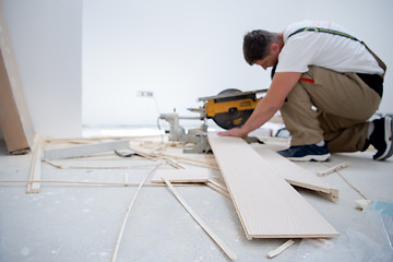 Image showing Man cutting laminate floor plank with electrical circular saw