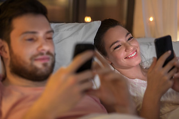 Image showing couple using smartphones in bed at night