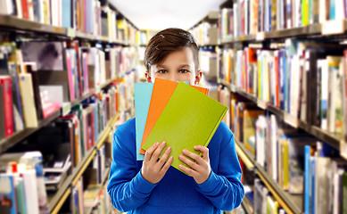 Image showing shy student boy hiding behind books at library