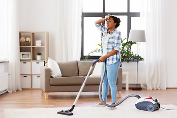 Image showing tired african woman with vacuum cleaner at home