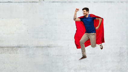 Image showing man in red superhero cape jumping over concrete