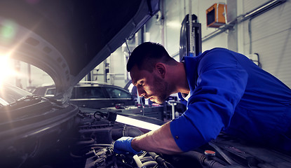 Image showing mechanic man with lamp repairing car at workshop