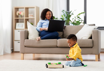 Image showing baby playing toy blocks and mother using laptop