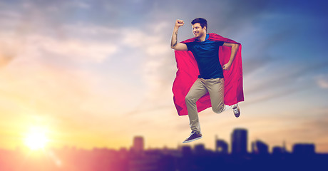 Image showing man in superhero cape flying over sunset in city