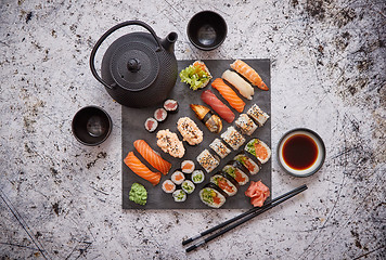 Image showing Assortment of different kinds of sushi rolls placed on black stone board