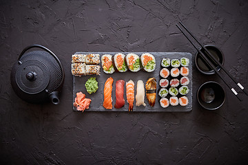 Image showing Assortment of different kinds of sushi rolls placed on black stone board