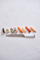 Image showing Various sushi rolls with Japanese knife on white stone slate background