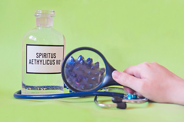 Image showing Ethanol in a bottle on the table with of microscope virus close up, stethoscope and loupe. Coronavirus concept Tablet in the fingers of hand