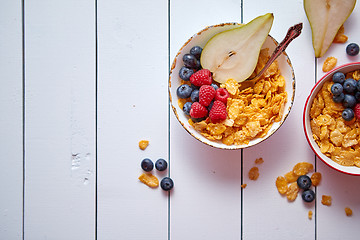 Image showing Golden cornflakes with fresh fruits of raspberries, blueberries and pear in ceramic bowl