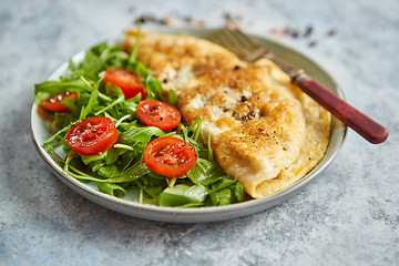 Image showing Classic egg omelette served with cherry tomato and arugula salad on side