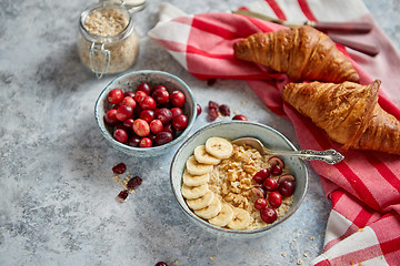 Image showing Ceramic bowl of oatmeal porridge with banana, fresh cranberries and walnuts