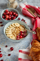 Image showing Ceramic bowl of oatmeal porridge with banana, fresh cranberries and walnuts
