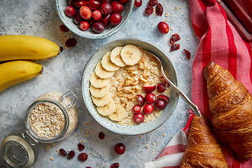 Image showing Ceramic bowl of oatmeal porridge with banana, fresh cranberries and walnuts