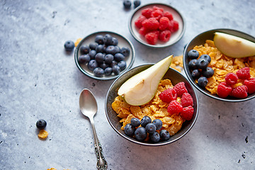 Image showing Golden cornflakes with fresh fruits of raspberries, blueberries and pear in ceramic bowl