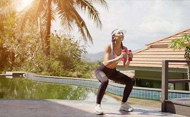Image showing Sportswoman squatting with dumbbells on poolside