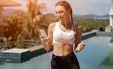 Image showing Smiling sportswoman listening to music near swimming pool