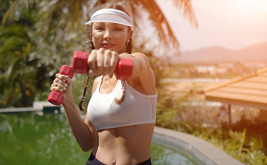Image showing Cheerful woman exercising with dumbbells near swimming pool