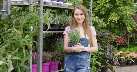 Image showing Young pretty gardener woman posing at stand with potted flowers