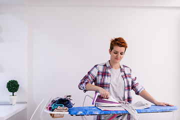 Image showing Red haired woman ironing clothes at home