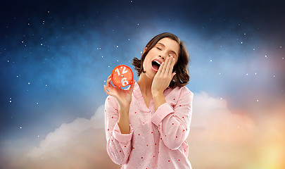 Image showing sleepy woman in pajama with alarm clock yawning