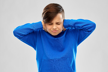 Image showing stressed boy in blue sweater closing ears by hands