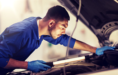 Image showing mechanic man with lamp repairing car at workshop