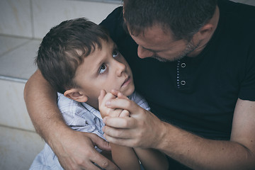 Image showing Portrait of young sad little boy and father sitting outdoors at 