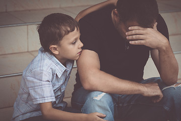 Image showing Portrait of young sad little boy and father sitting outdoors at 