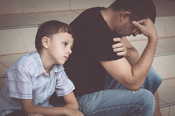 Image showing Portrait of young sad little boy and father sitting outdoors at 