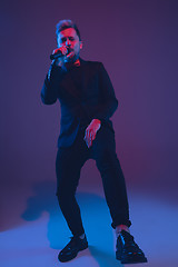 Image showing Young caucasian musician, performer singing, dancing in neon light on gradient background