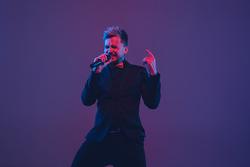 Image showing Young caucasian musician, performer singing, dancing in neon light on gradient background