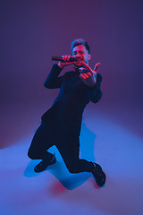 Image showing Young caucasian musician, performer singing, dancing in neon light on gradient background