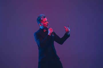 Image showing Young caucasian musician, performer singing, dancing in neon light on gradient background