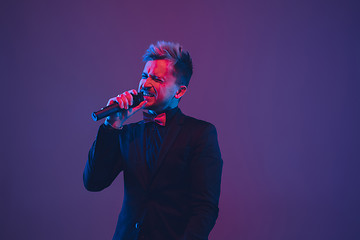 Image showing Young caucasian musician, performer singing, dancing in neon light on gradient background