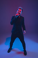 Image showing Young caucasian musician, performer singing, dancing in neon light on gradient background