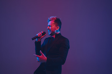 Image showing Young caucasian musician, performer singing, dancing in neon light on gradient background