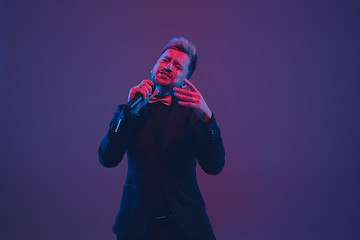 Image showing Young caucasian musician, performer singing, dancing in neon light on gradient background